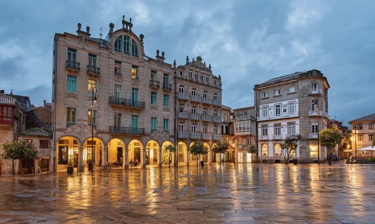 The Praza da Ferrería in Pontevedra, with lit arcades and wet paving at dusk